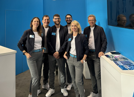 Messeteam von SKZ in einheitlicher Messebekleidung: dunkle Bomberjacken, weiße Shirts und graue Hosen mit blauen Gürteln vor blauer Messewand